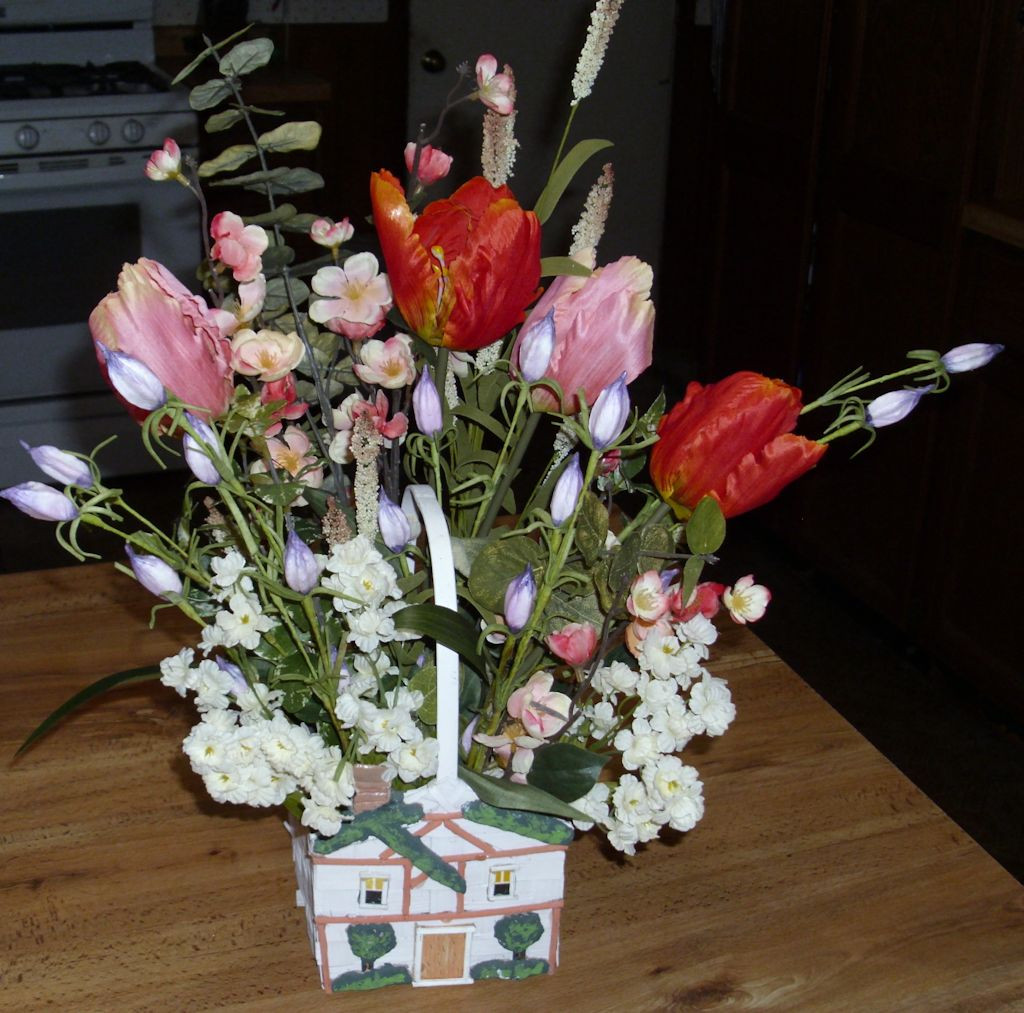 A flower basket in the shape of a house with a springtime arrangement.
